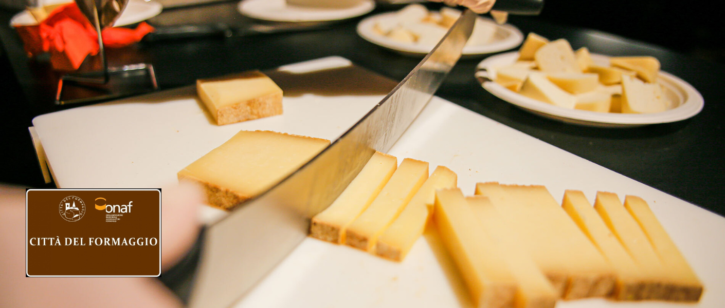 Taglio e assaggio del formaggio, con il riconoscimento Città del Formaggio interamente visibile nella fotografia originale